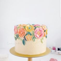 a white cake with pink and yellow flowers on it sitting on a gold plated stand