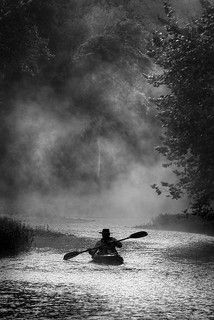 a person in a kayak paddling down a river on a foggy day