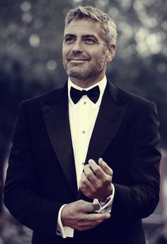 a man in a tuxedo is smiling and holding his hands together