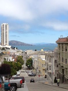 a city street with cars parked on both sides and buildings along the side, overlooking water