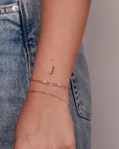 a woman's wrist with a small initial tattoo on the left side of her arm