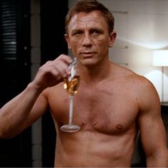 a shirtless man holding a wine glass in his right hand and looking at the camera