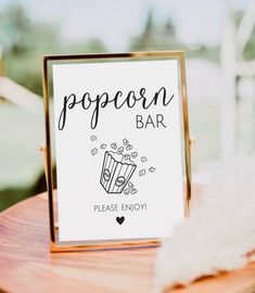 a popcorn bar sign sitting on top of a wooden table next to a white feather