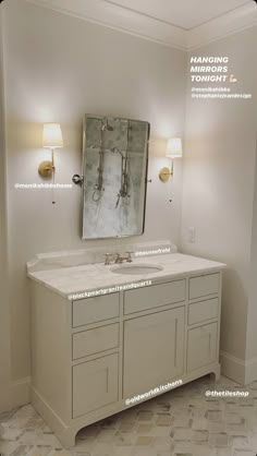 a bathroom vanity with two lights and a large mirror above it, in front of a white wall