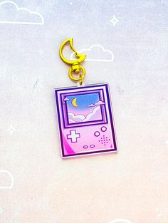 a gameboy keychain hanging from a hook on a white surface with clouds and stars