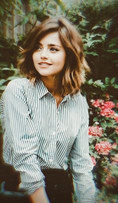 a woman is sitting in front of some flowers and bushes with her hands on her hips