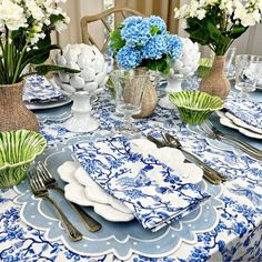 a blue and white table setting with flowers in vases on the side, plates and silverware