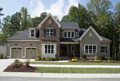 a large gray house with two garages and lots of trees in the front yard