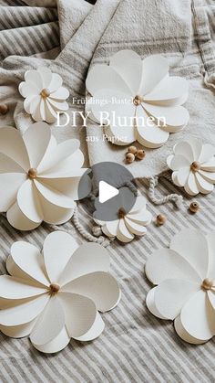 white paper flowers sitting on top of a bed next to a pillow and blanket with the words diy bluuten