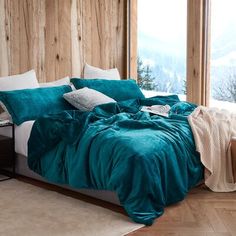 a bed covered in teal colored sheets and pillows with blankets on top of it