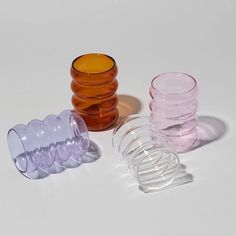 three different colored glass cups sitting next to each other on a white surface with shadows coming from them