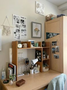 a wooden desk topped with lots of clutter next to a wall mounted art piece