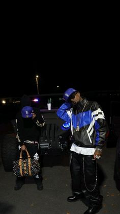 two men standing next to each other in front of a truck at night, one holding a handbag and the other carrying a purse