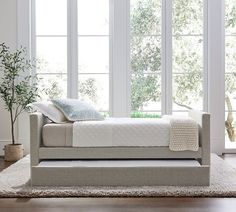 a white bed sitting on top of a wooden floor next to two windows with lots of windows