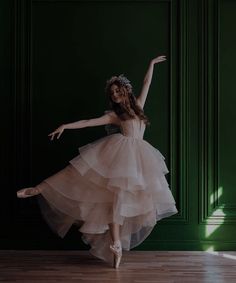 a woman in a dress is dancing on a wooden floor with green walls behind her