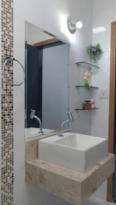 a white sink sitting under a bathroom mirror next to a shelf with flowers on it