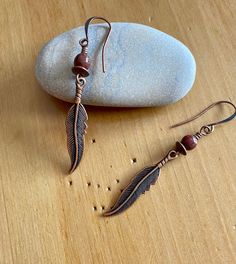 "lost & found ~ etched antique copper finished feather charm earrings with sage green speckled burgundy red and copper accents Details & measurements: ~ Beautifully detailed antique copper finished feather charms (8 x 36mm) ~ Accented by saucer shaped copper spacer beads (6 x 2mm) and Czech Glass round beads in burgundy red w/ splattered sage green Picasso finish (6mm) ~ They hang from antique copper ear wires ~ Earrings hang just over 2 1/2\" long ♡ Packaged safely & sustainably in a kraft box with cotton ribbon & dried organic florals. This makes for a beautiful gift, or something pretty for yourself! All packaging materials are zero waste and also reusable. ♡ As well, we always aim to ship with plastic-free packing materials. Sustainability is an integral part of our lives, and we bring