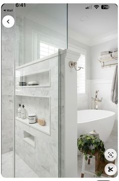 a bathroom with white marble walls and flooring, along with a bathtub in the corner