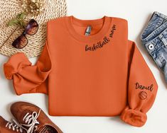 an orange sweatshirt with writing on it next to some shoes and a straw hat, sunglasses