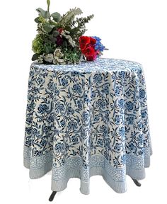 a blue and white table cloth with red flowers on it next to a potted plant