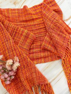 an orange scarf with fringes and flowers sitting on a white table next to it