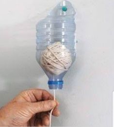 a hand holding a ball of yarn on top of a string attached to a water bottle