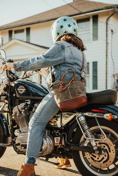 a woman riding on the back of a motorcycle wearing a denim jacket and jeans pants