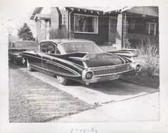 an old black and white photo of two cars parked in front of a brick house