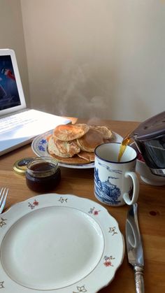 a laptop computer sitting on top of a wooden table next to plates and silverware