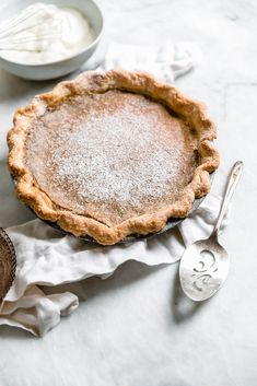 a pie sitting on top of a white table next to a spoon and bowl filled with whipped cream