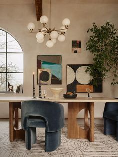 a dining room table with chairs and art on the wall behind it, along with two large windows