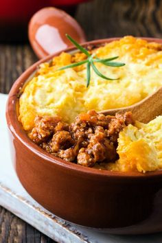 a wooden spoon is in a dish with meat and cheese on the table next to a red pot