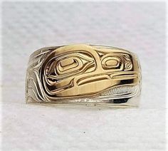 On offer is a made to order West Coast Namgis First Nation Hand carved sterling silver with 14k gold overlay ''Raven'' ring. by World renowned master carver Joe R. Wilson with his depiction of Raven in the style of the Namgis, Kwakuitl First Nation. Initialed by Joe. Fine example of Indigenous Art from the Northwest Coast First Nations of Canada. PLEASE NOTE THAT THIS IS A CUSTOM RECREATED HAND CARVED ITEM THAT WILL HAVE SLIGHT, SUBTLE DIFFERENCES THAT ARE VERY HARD TO DISTINGUISH WHEN COMPLETED Symbolic Carved White Gold Jewelry, Symbolic Carved Jewelry For Formal Occasions, Carved Symbolic Yellow Gold Jewelry, Ceremonial Sterling Silver Engraved Ring With Polished Finish, Yellow Gold Symbolic Carved Jewelry, Symbolic Carved Gold Jewelry, Unique Carved Yellow Gold Ring, Carved Sterling Silver Heirloom Jewelry, Gold Sterling Silver Rings With Etched Details