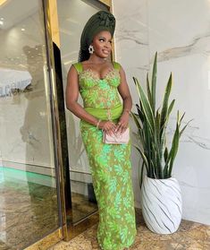 a woman in a green dress standing next to a plant