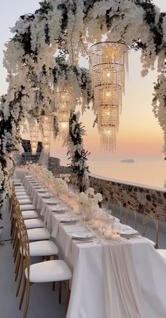 a long table with white flowers and chandelier hanging from it's ceiling