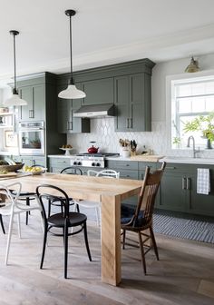 a kitchen with green cabinets and wooden table surrounded by chairs in front of an oven