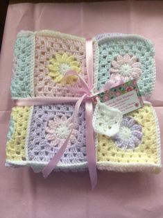 three crocheted squares are wrapped in pink ribbon