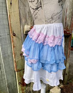 "a short white cotton skirt  tiered, & with blue silk georgette ruffles that are higher at the back  featuring a vintage embroidery on linen of a lady with flowers centre front  embellished with pink cotton blend lace and small mmf daisy motifs SIZE the elastic waist stretches from 66 cm /?26\" to  94 cm / 37\" length is 43cm / 17\" mannequin is size small / m gentle wash" White Tiered Skirt Petticoat For Summer, Summer Cotton Petticoat With Ruffles, Summer Cotton Petticoat With Attached Cancan, White Ruffled Petticoat With Flowy Fit, Summer Tiered Petticoat With Attached Cancan, White Tiered Petticoat For Summer, Ruffled Mini Skirt For Garden Party, Summer Cotton Skirt With Attached Cancan, Spring Cotton Petticoat With Ruffles