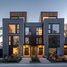 two story house with large windows and lots of plants on the front lawn at dusk