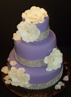 a three tiered purple cake with white flowers on top