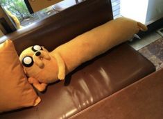 a stuffed animal laying on top of a brown couch next to a pillow with eyes