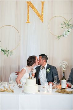 a bride and groom kissing in front of a cake with the letter n on it