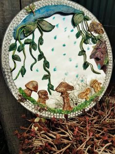 a plate that has been decorated with mushrooms and plants on it, sitting in the grass