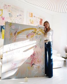 a woman standing next to a large painting in a room with white walls and flooring