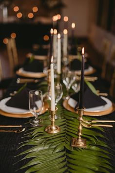 the table is set with black and gold place settings, candles, and fern leaves