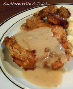 a white plate topped with meat and gravy covered in gravy next to mashed potatoes