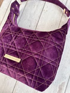 "This purple velvet quilted shoulder bag is a standout classic, with a modern twist - the unique touches include the asymmetrical strap and striking quilting pattern on the front and back. The gold accents really make this bag stand out.  This bag will be a perfect date night bag, with cozy vibes and sophisticated jewel tones that will complete any outfit be it out for brunch or cocktails.  The interior features a zip pocket and 2 slip pockets in a designer purple fabric print from Laura Miller's Moody Blooms collection.  Handbag size: 10\" W x 8\" H x 4-1/2\" D" Elegant Purple Bags With Zipper Closure, Everyday Purple Bags With Gold-tone Hardware, Elegant Purple Bags With Gold-tone Hardware, Fancy Handbags, Velvet Handbag, Designer Purple Bags With Gold-tone Hardware, Purple Shoulder Bag With Gold-tone Hardware And Double Handle, Quilted Shoulder Bag, Party Handbags