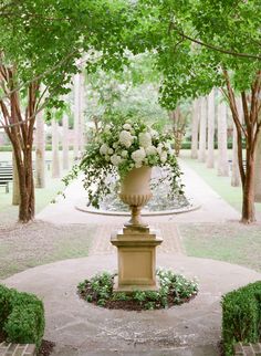 a large vase filled with white flowers sitting on top of a stone walkway next to trees