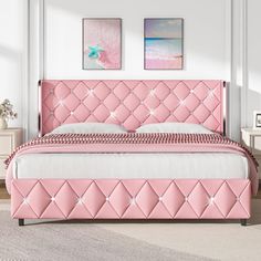 a pink bed in a white room with two pictures on the wall and a rug