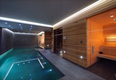 an indoor swimming pool surrounded by wooden walls and flooring with lights on the ceiling